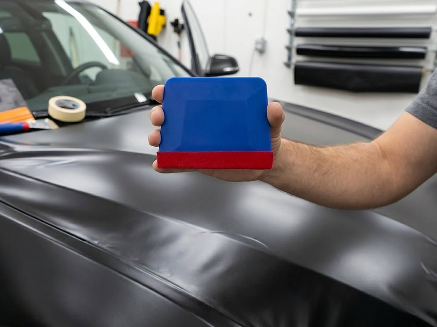 Hexis MARBLEU blue vinyl squeegee with red felt edge held by installer for wrap and tint application